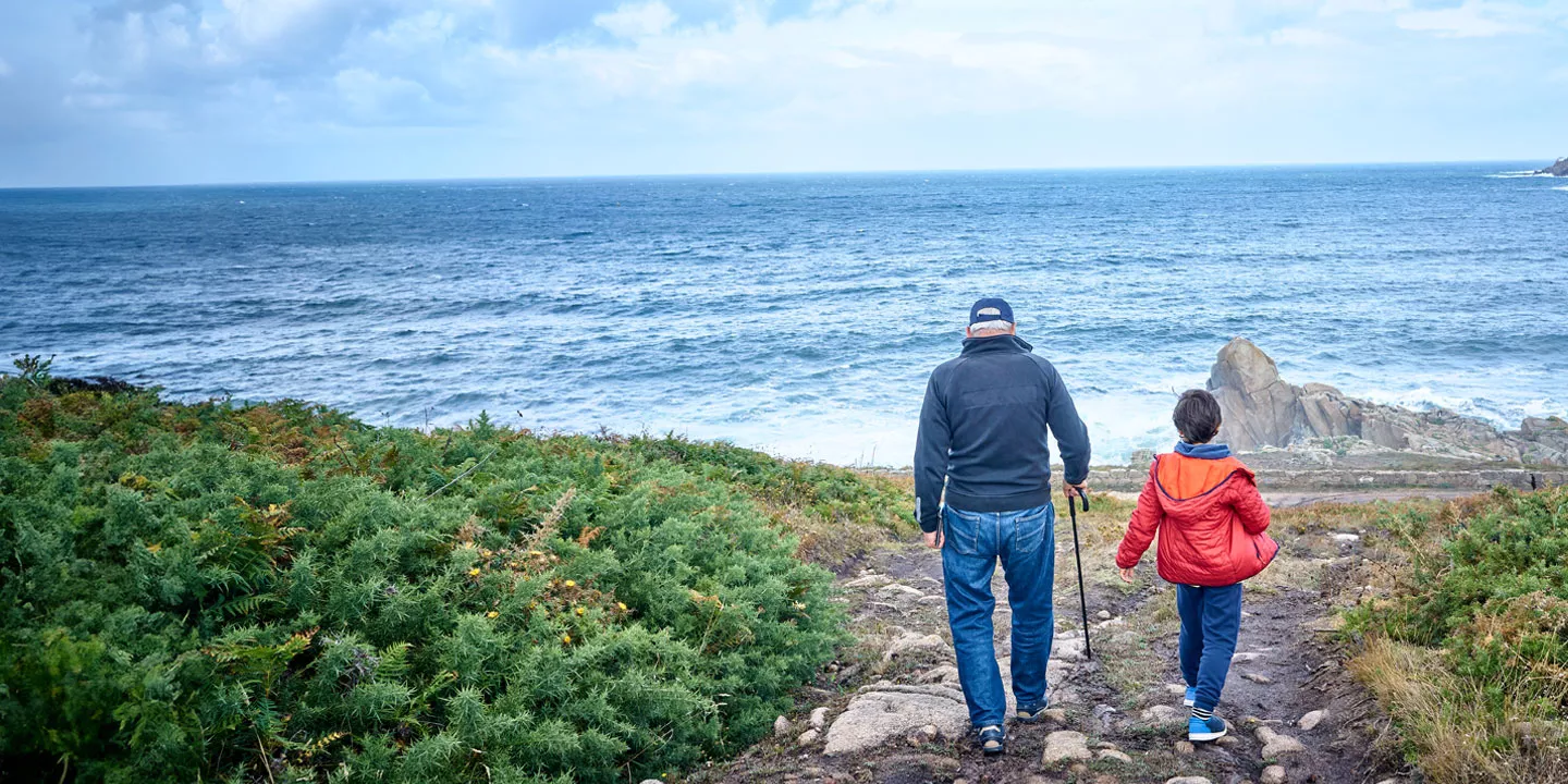 A grandfather and child walking towards the water on a coastal path