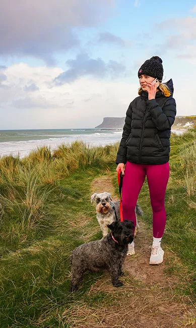 Young woman on phone while walking dogs along the coast