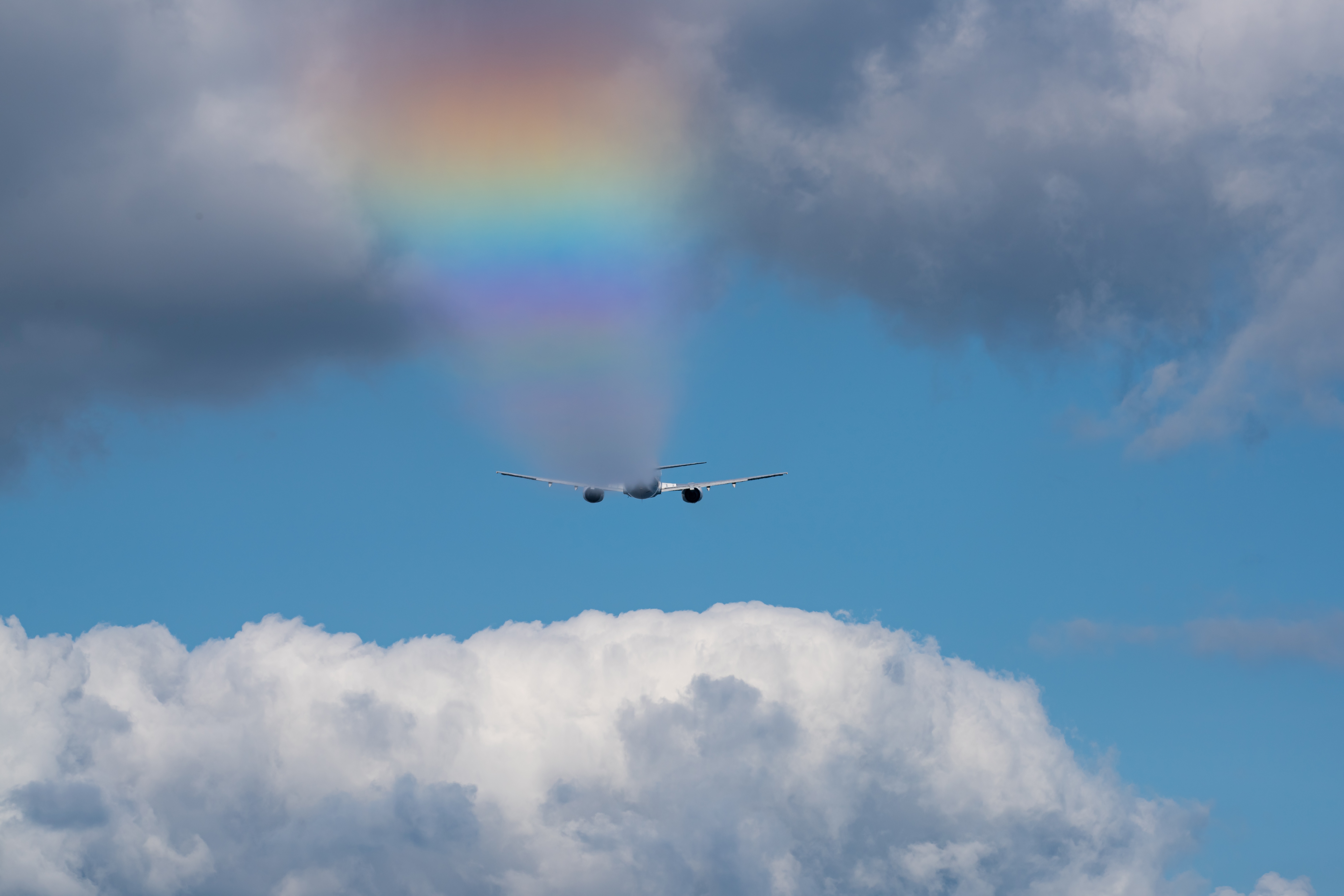 A large jet type plane spraying dispersant over water, creating a rainbow effect in the air