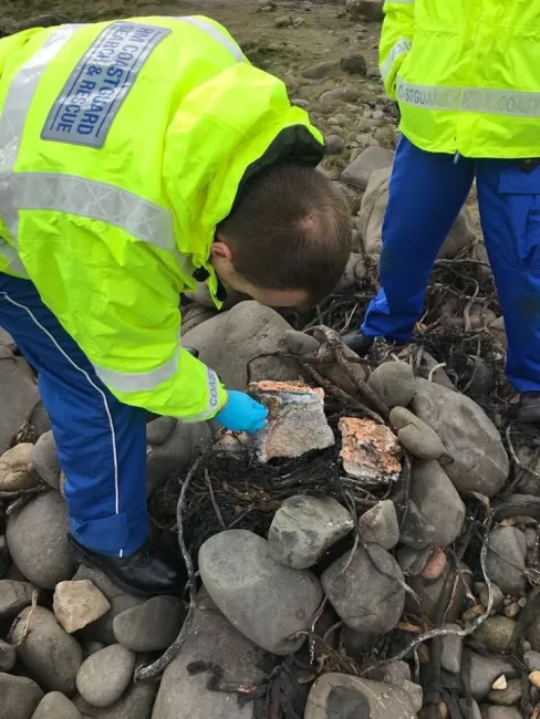 A Coastguard rescue officer inspects possible palm oil on a rocky beach
