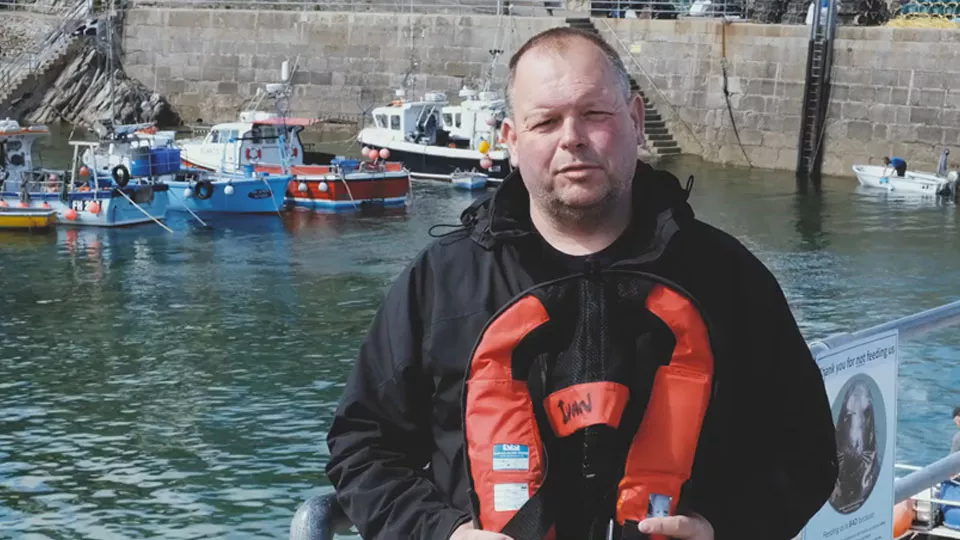 A man wearing a PFD stands by the waterside at a harbour