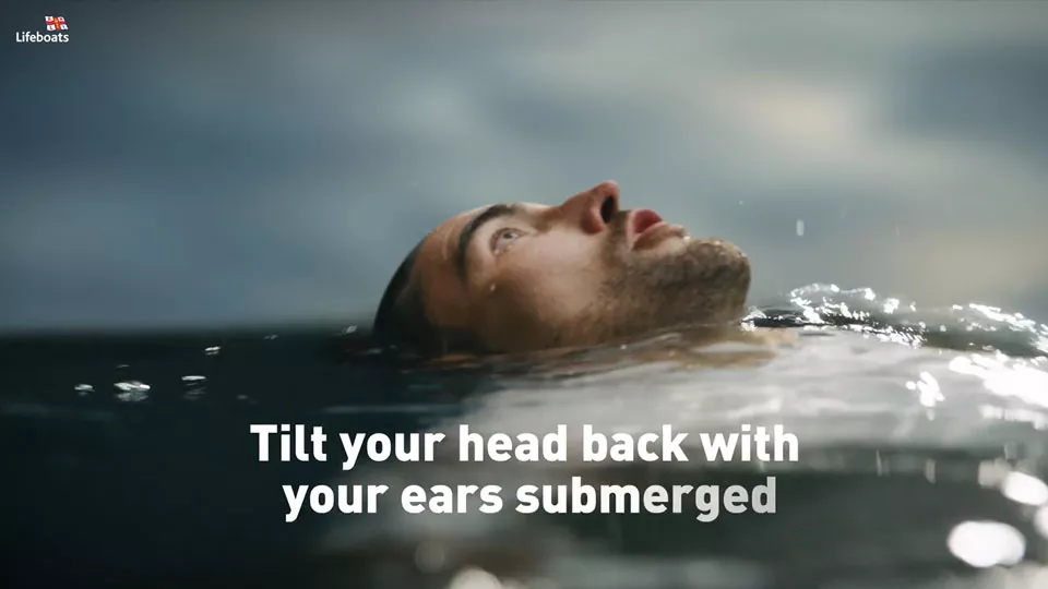 A man floats in water with his head back and ears submerged below the waterline