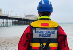 Coastguard rescue officer standing on the shore looking at the sea and pier in background
