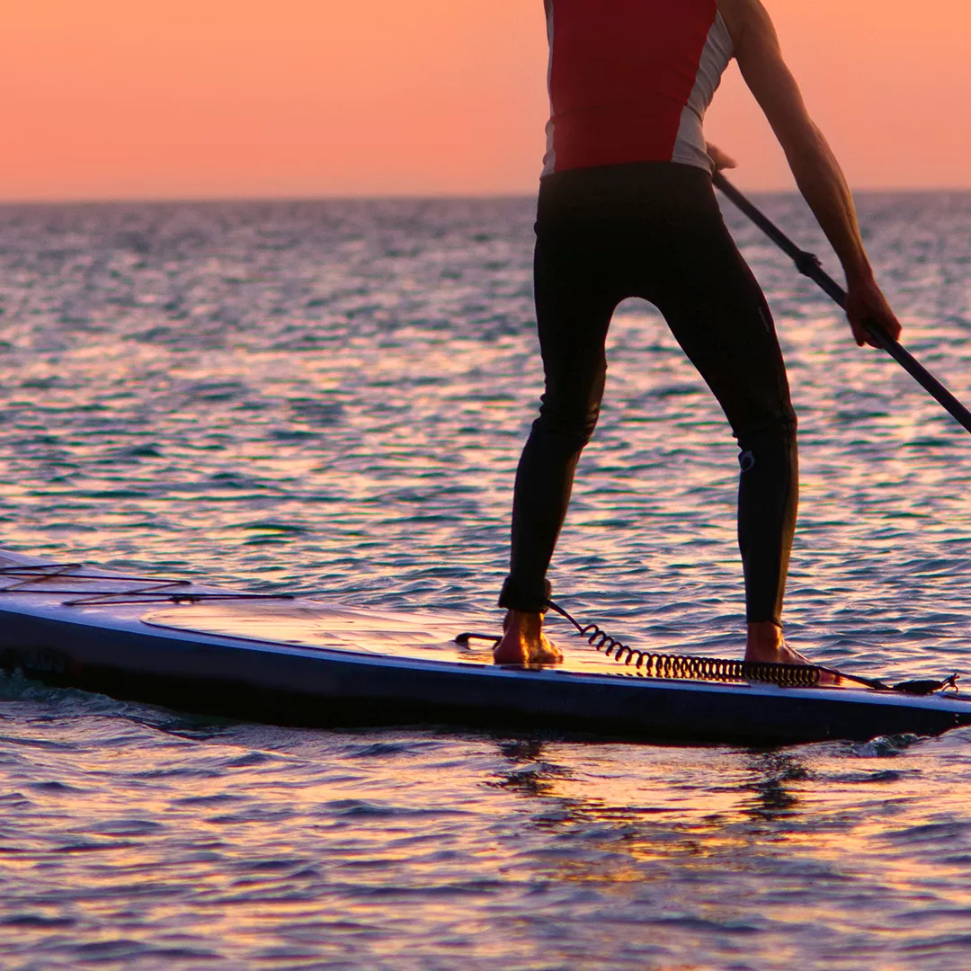 A man paddleboarding at sunset