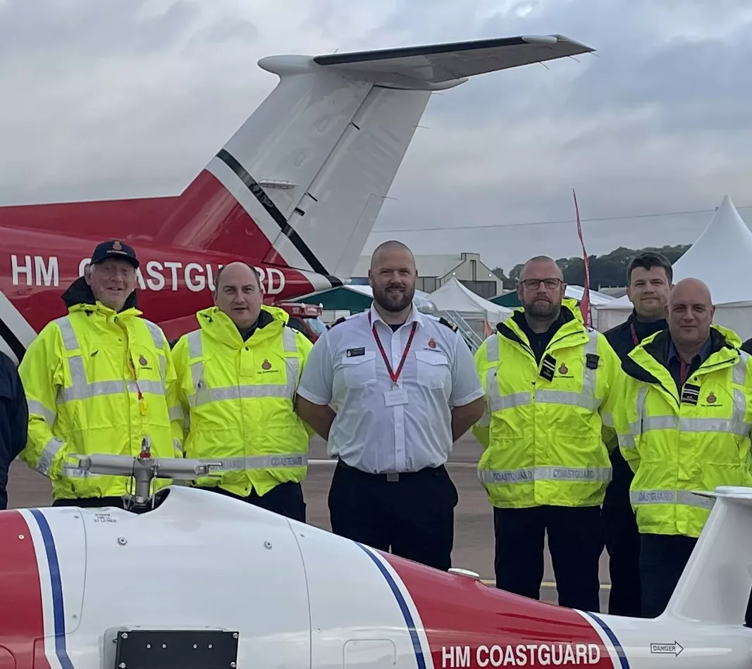 Five men stood between two HM Coastguard aircraft, one man in white shirt between four in high-vis jackets