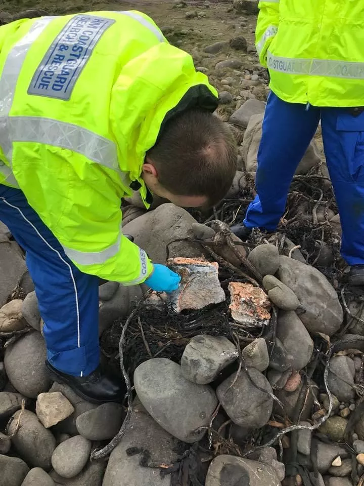 Man in high vis carefully examining a white substance on rocky pebbles