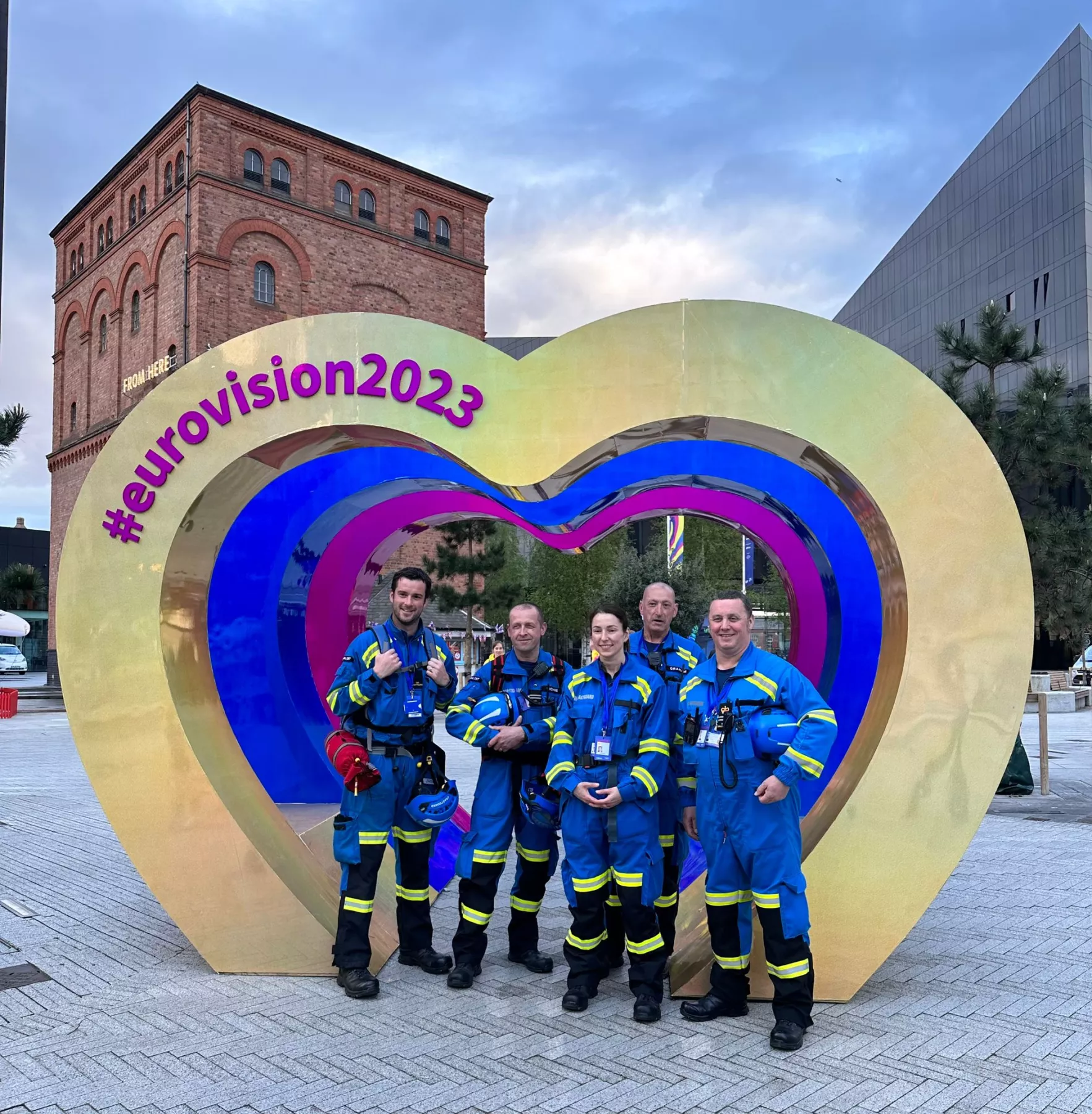 Five coastguards in uniform posing in front of Eurovision stand in Liverpool